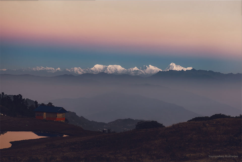 An orange sky hovers above snow-covered mountains. A blurry line
divides the orange sky from a darker sky. In the foreground are hills
and a house.
Please see the explanation for more detailed information.