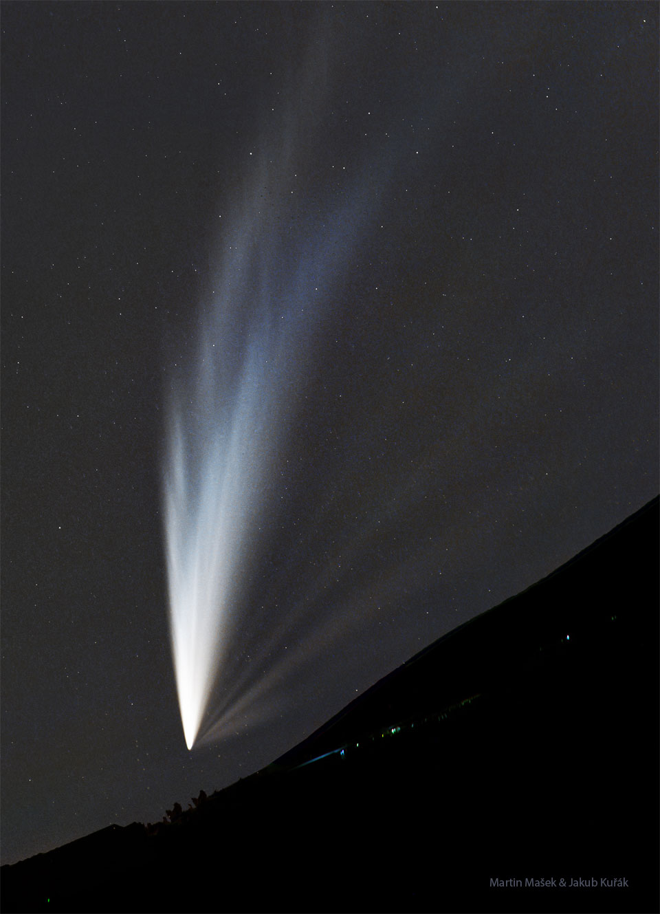 A dark sloping hill is seen at the bottom with a 
bright comet with many tails visible above it, taking
up most of the frame. The tails closest to the slope 
are the most dim. 
Please see the explanation for more detailed information.